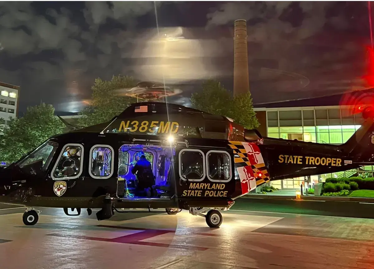 Maryland State Police helicopter parked at night with cabin lights glowing and rotor blur.
