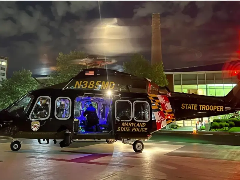 Maryland State Police helicopter parked at night with cabin lights glowing and rotor blur.