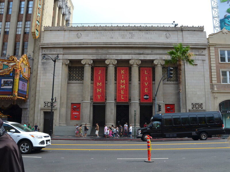 Historic theater facade with red banners and pedestrians on a city street.