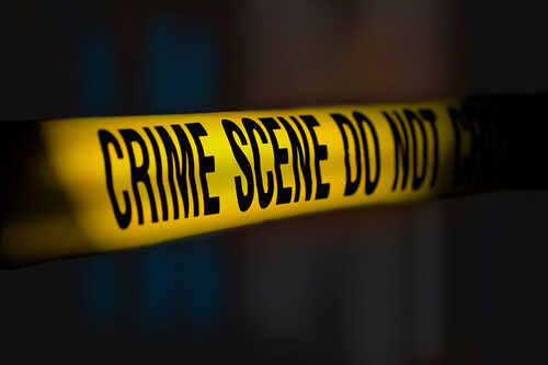 Yellow crime scene tape with bold black lettering stretched across a dark background.
