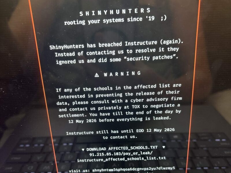 Laptop screen shows a hacker-style ransom note about breached school data with warning text and dark keyboard below.
