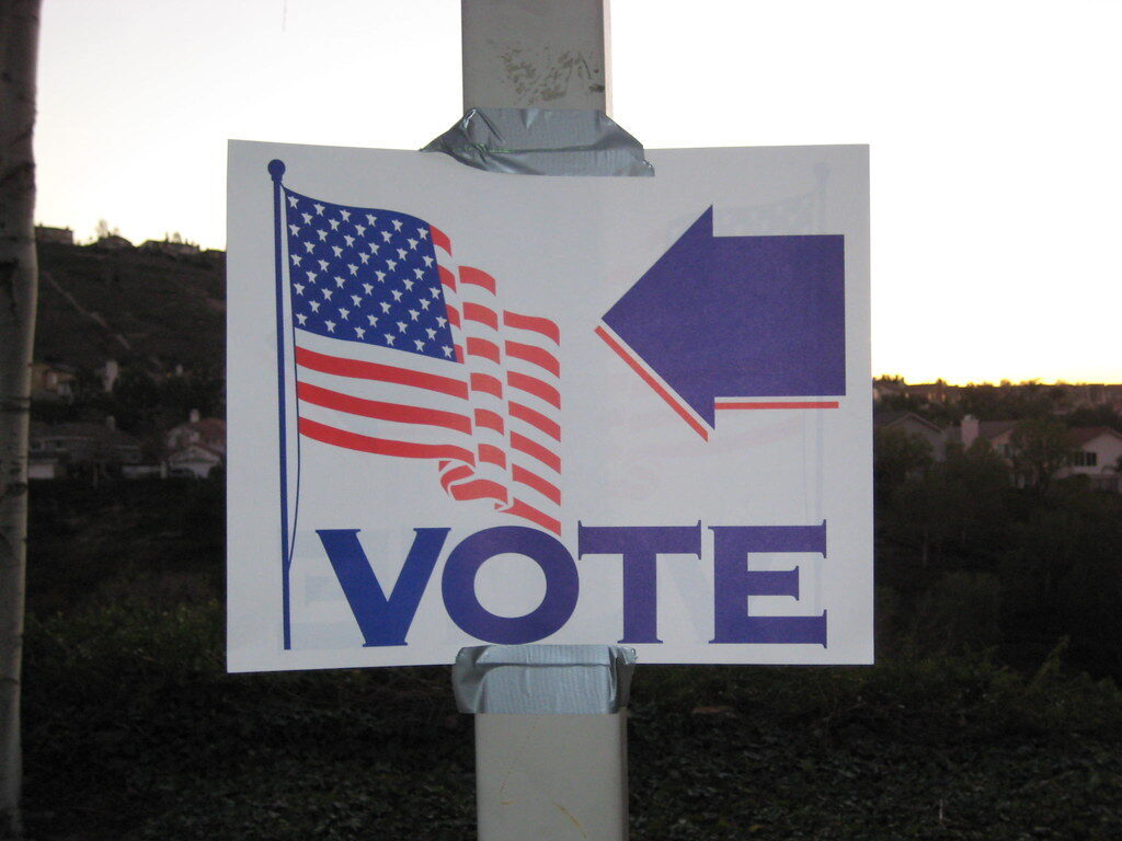 Handmade vote sign with an American flag and purple arrow taped to a pole at dusk.