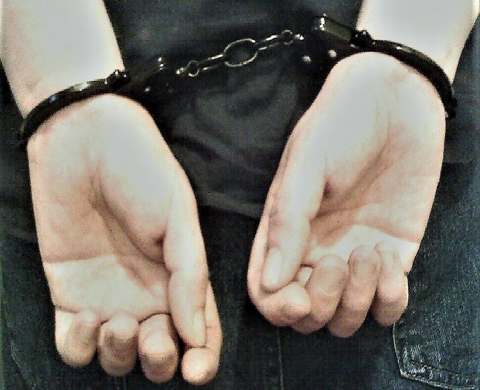Person's hands cuffed behind their back with black leather restraints.