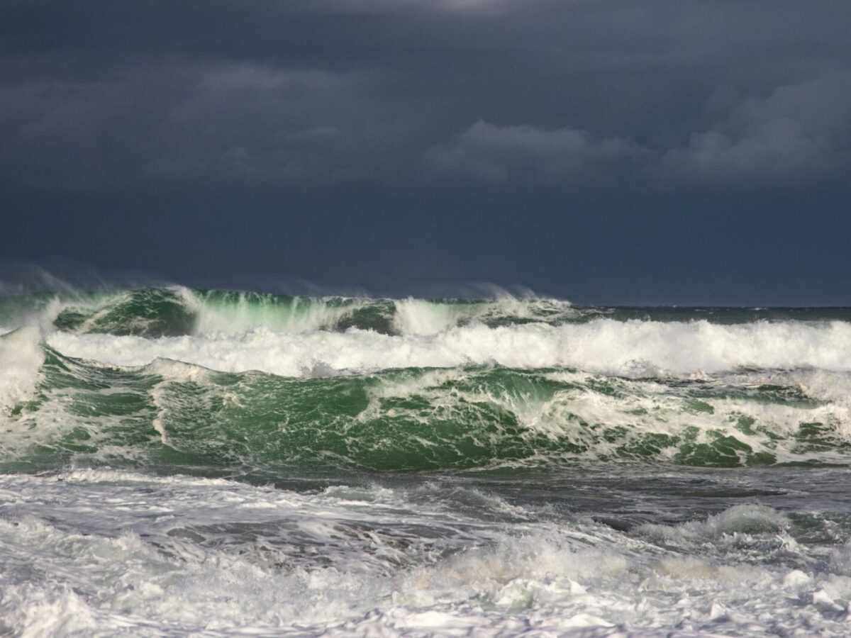 Powerful ocean waves crash under dark stormy clouds, capturing nature's raw force.