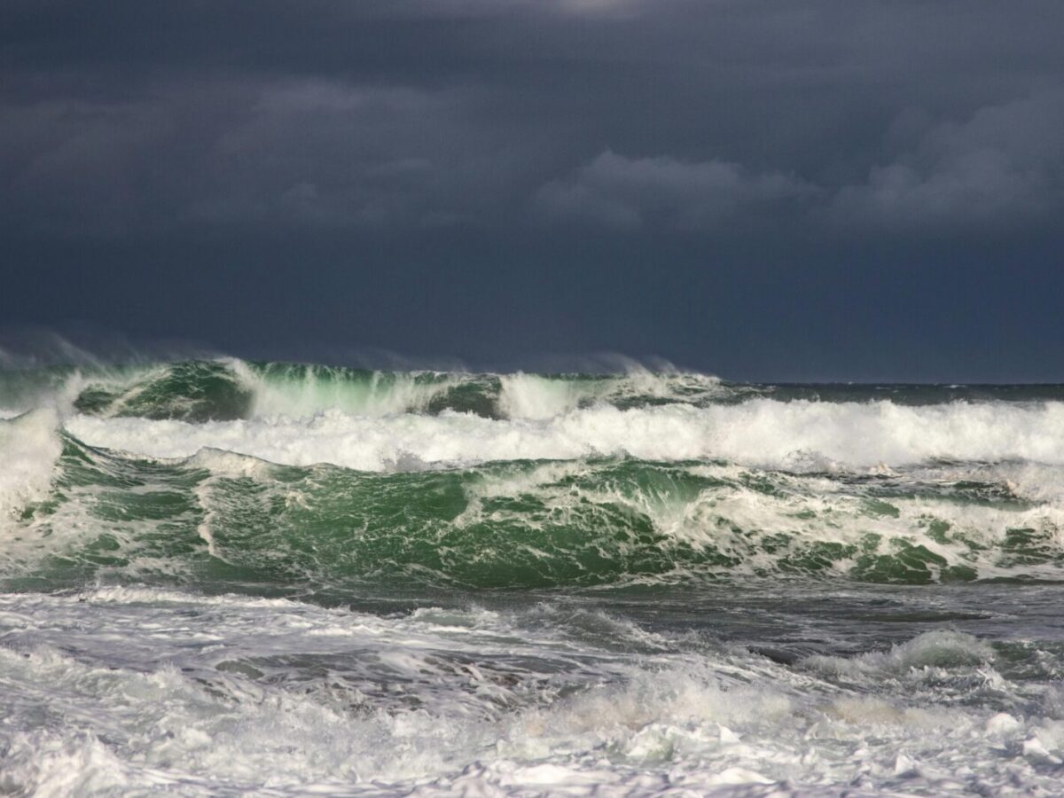 Powerful ocean waves crash under dark stormy clouds, capturing nature's raw force.