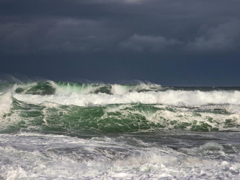 Powerful ocean waves crash under dark stormy clouds, capturing nature's raw force.