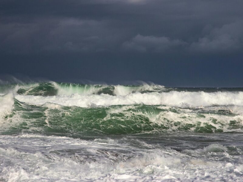 Powerful ocean waves crash under dark stormy clouds, capturing nature's raw force.