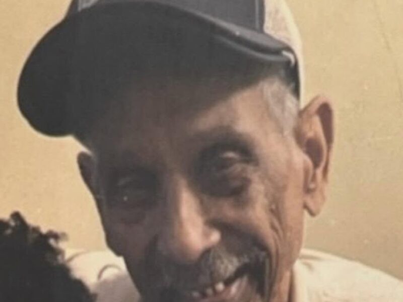 Close-up of an elderly man wearing a black baseball cap and smiling indoors.