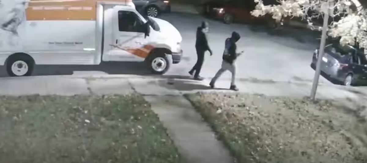 Two people walk past a parked white moving van on a nighttime street.