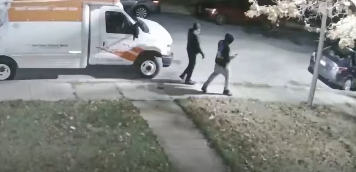 Two people walk past a parked white moving van on a nighttime street.