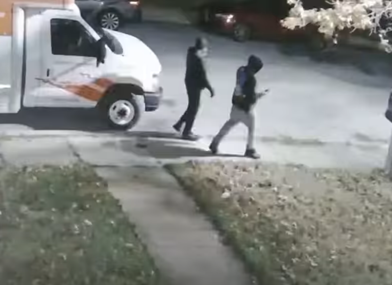 Two people walk past a parked white moving van on a nighttime street.