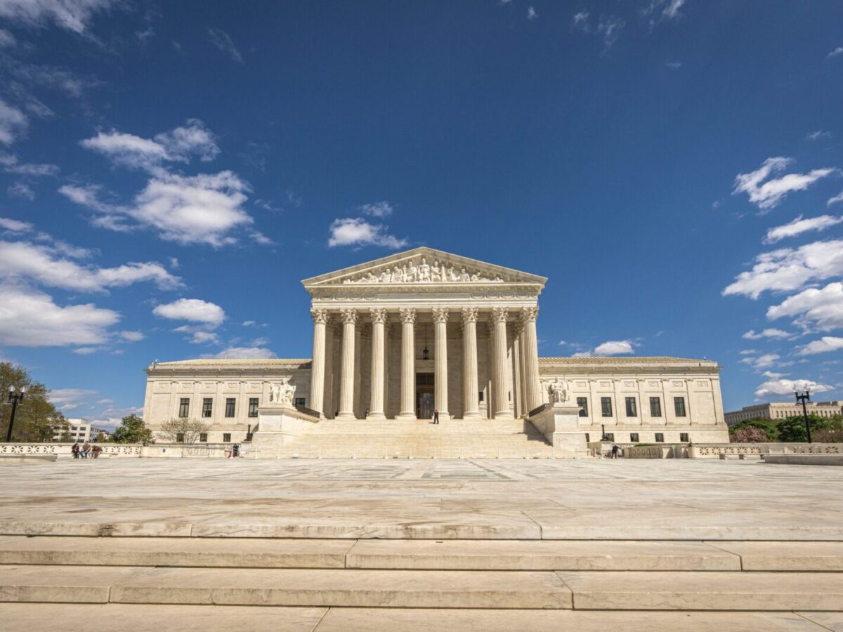Front view of the United States Supreme Court building on a sunny day with blue sky and clouds.