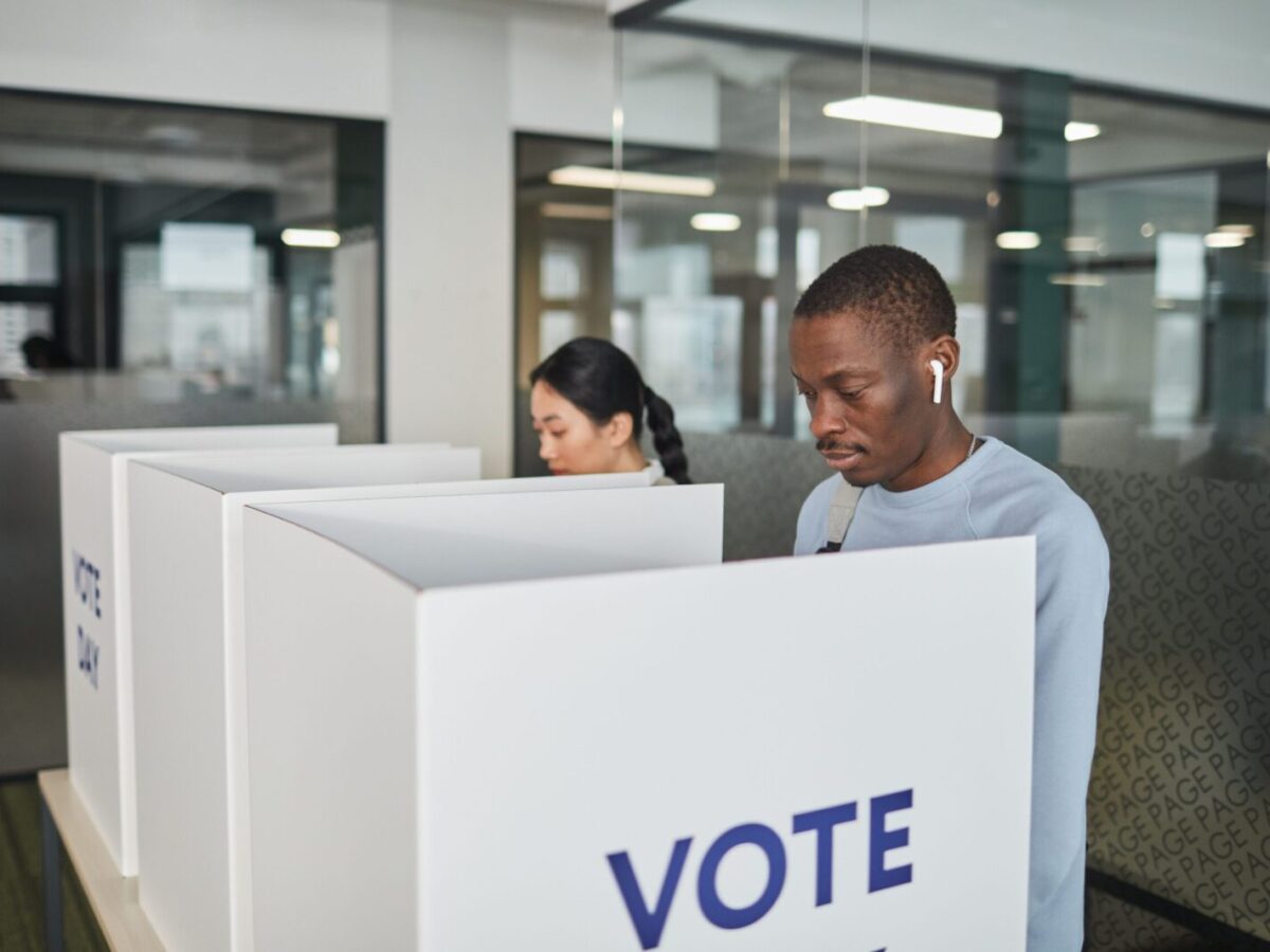Two individuals casting votes in an indoor voting booth, emphasizing democracy.