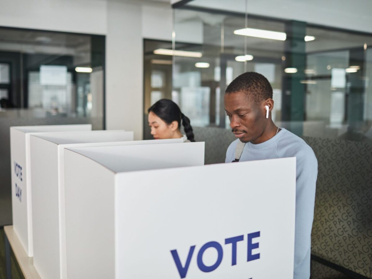 Two individuals casting votes in an indoor voting booth, emphasizing democracy.