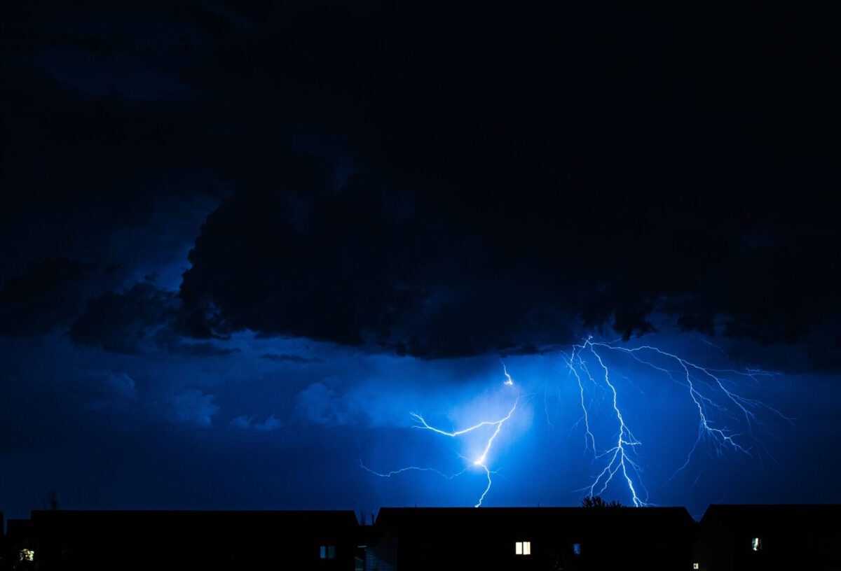 Powerful lightning illuminates the night sky during a storm, casting silhouettes over city rooftops.