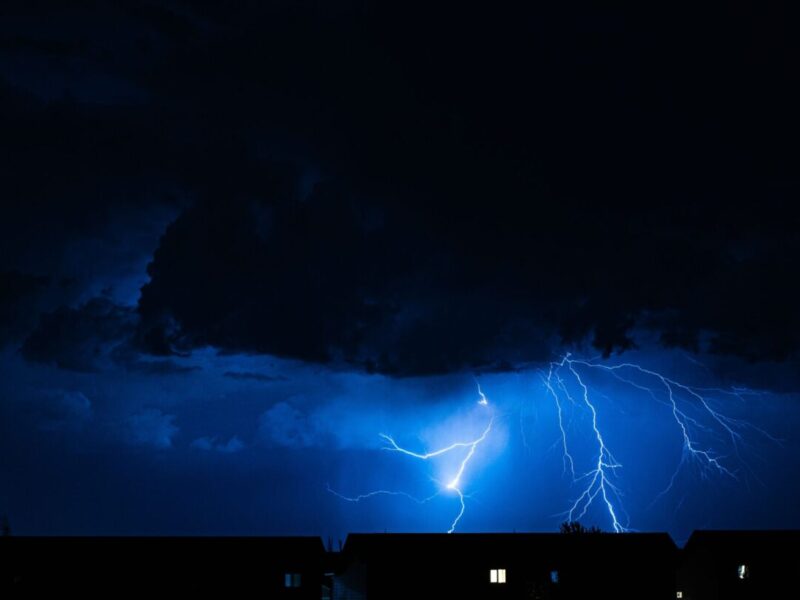 Powerful lightning illuminates the night sky during a storm, casting silhouettes over city rooftops.