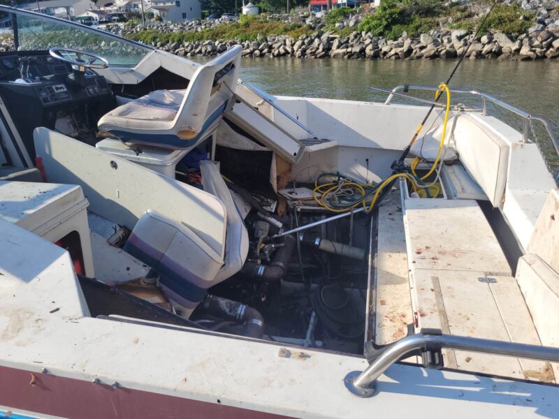 Abandoned boat interior with damaged seats, exposed wiring, and machinery by a harbor.
