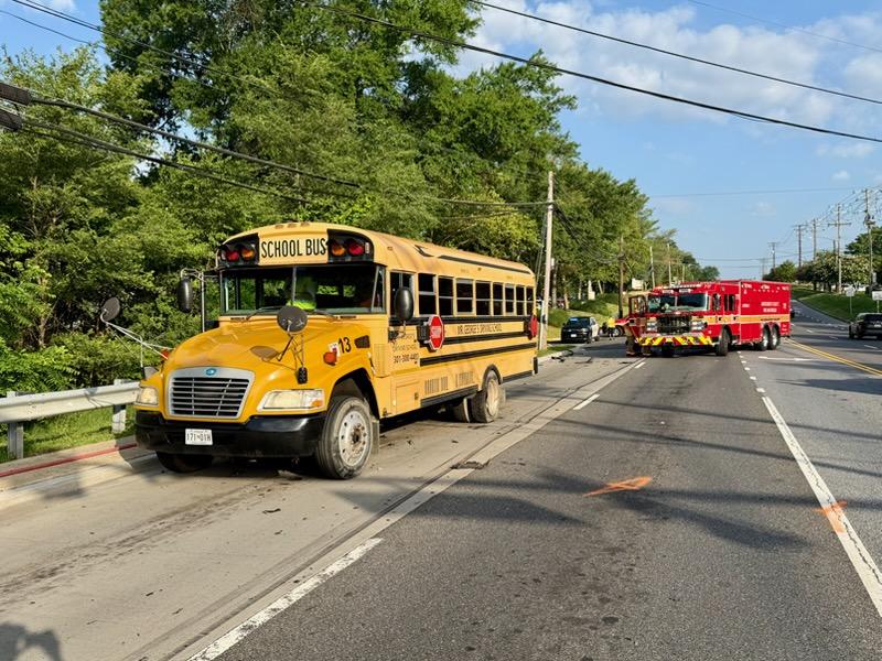 School bus and emergency trucks stopped on a suburban road after an incident.