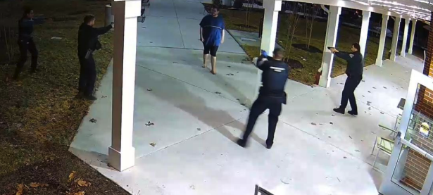 Several people stand and move around a lit porch and walkway at night, with one person in blue near the center.