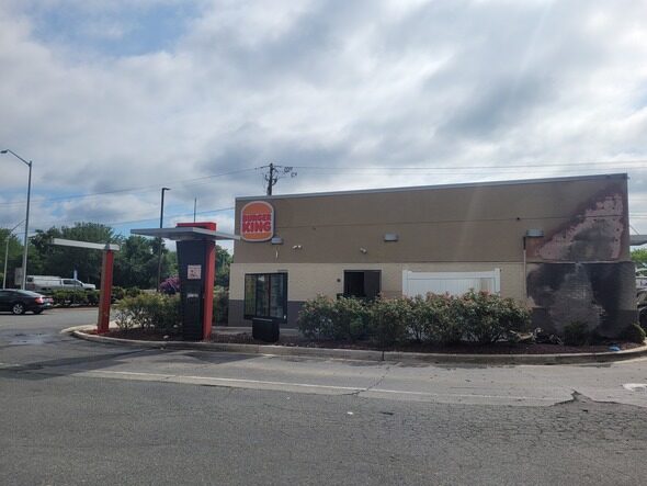 Abandoned Burger King restaurant with peeling exterior paint beside an empty drive-thru lane under a cloudy sky.