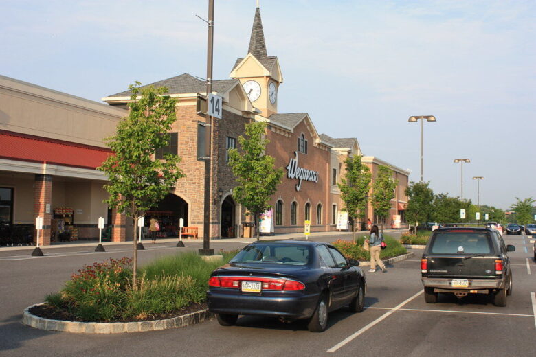Wegmans storefront in a suburban shopping center with parked cars and a clock tower.