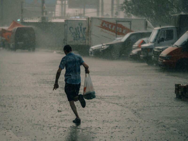 A man runs on a wet street carrying a plastic bag during heavy rain, creating a dramatic city scene.