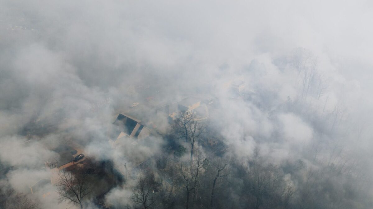 Aerial shot of a neighborhood shrouded in smoke, obscuring houses and trees.
