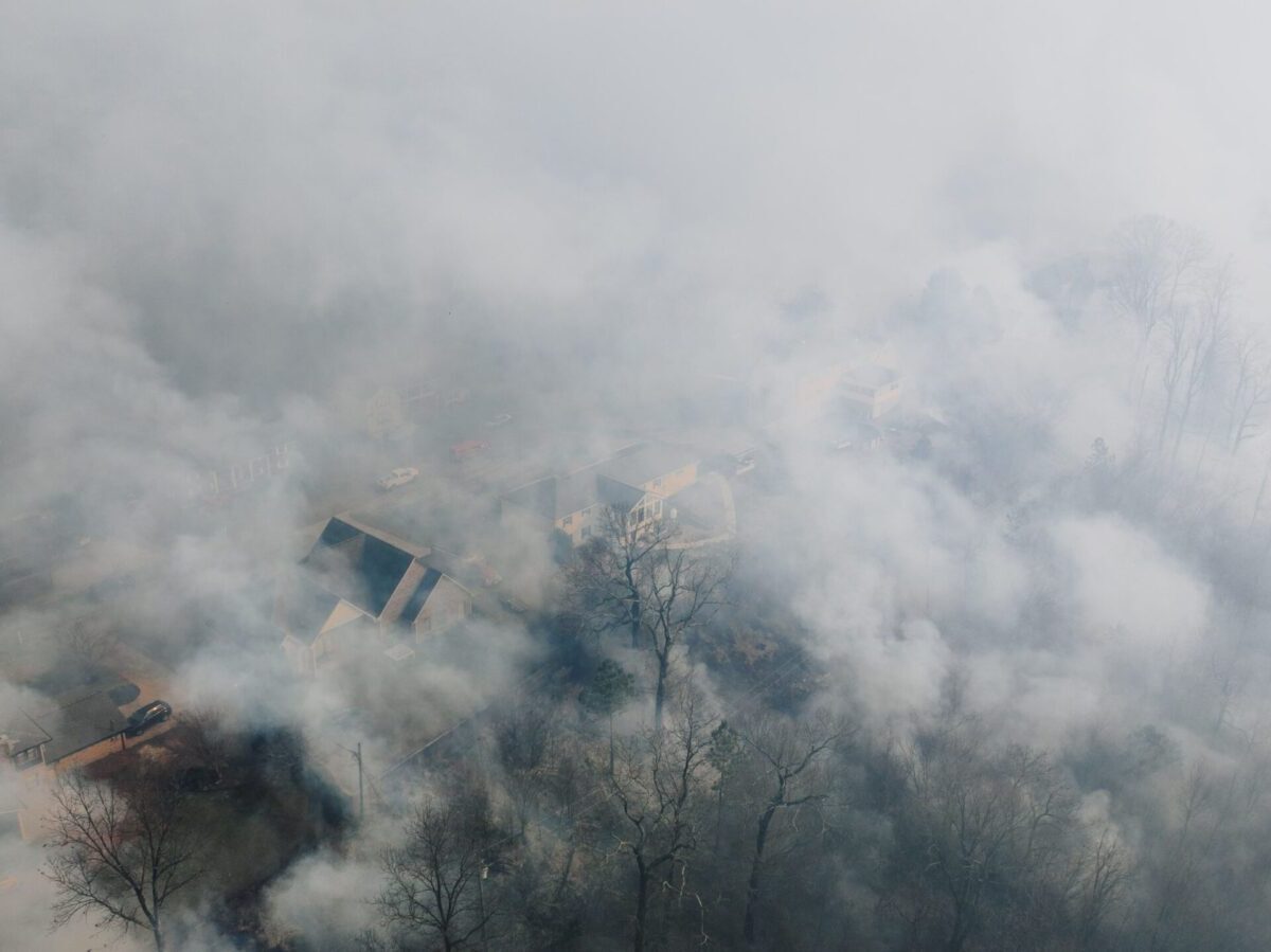 Aerial shot of a neighborhood shrouded in smoke, obscuring houses and trees.
