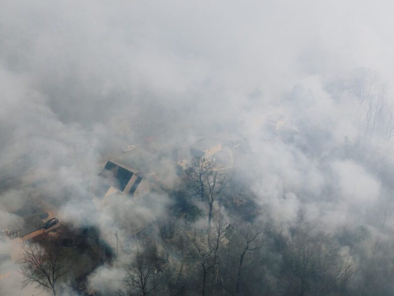 Aerial shot of a neighborhood shrouded in smoke, obscuring houses and trees.