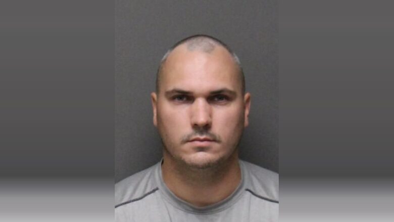 Neutral mugshot-style portrait of a bald man against a gray background.