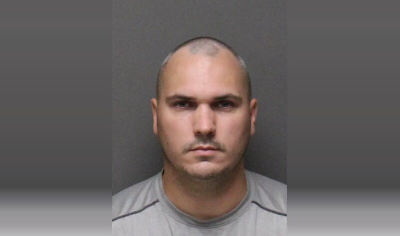 Neutral mugshot-style portrait of a bald man against a gray background.