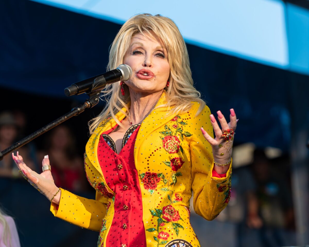 Blonde singer performing at a microphone in a bright yellow and red stage outfit