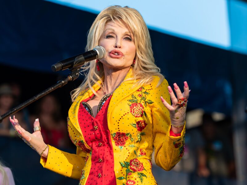 Blonde singer performing at a microphone in a bright yellow and red stage outfit