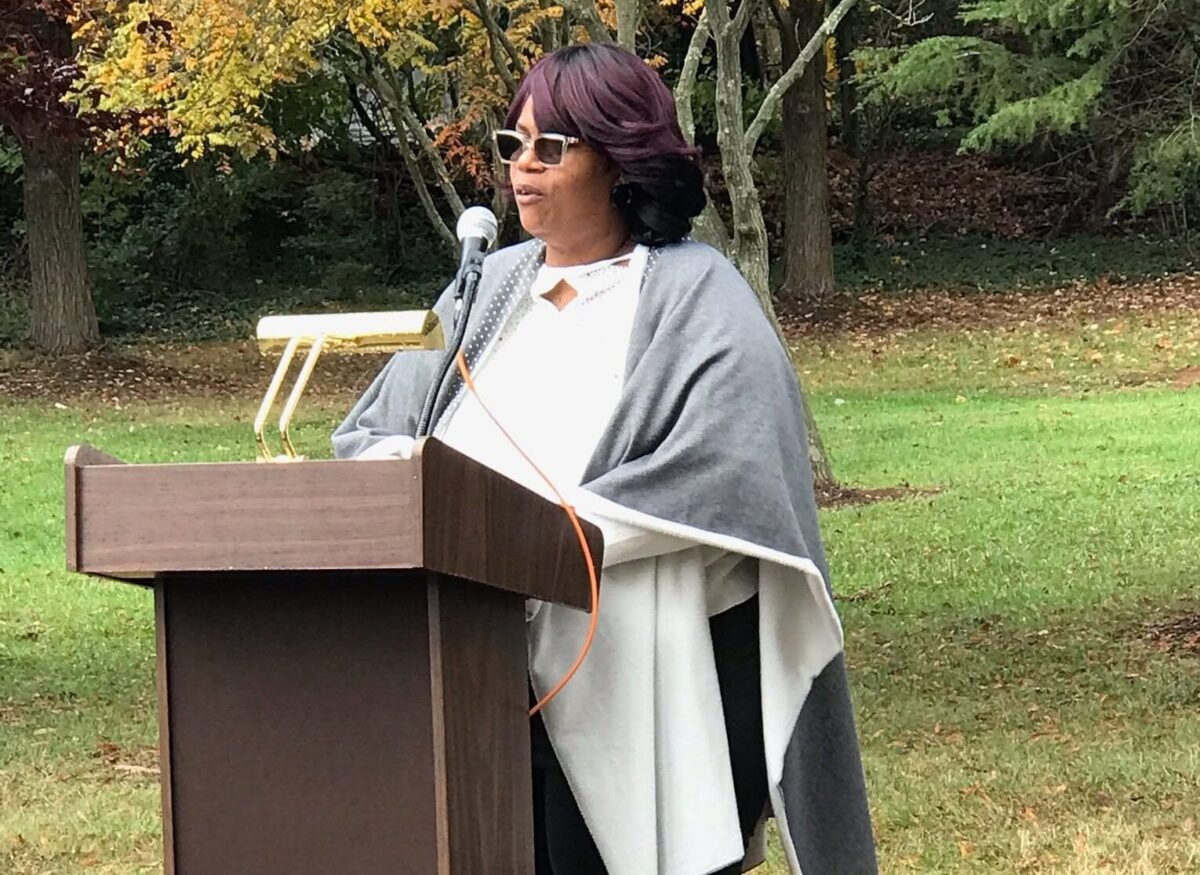 Woman speaking at a podium outdoors in a park during a ceremony.