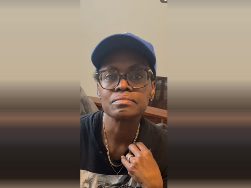 Person wearing glasses and a blue cap looks at the camera indoors.