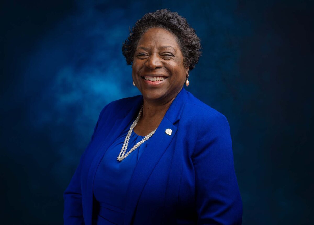 Smiling woman in a royal blue suit against a dark blue studio backdrop.
