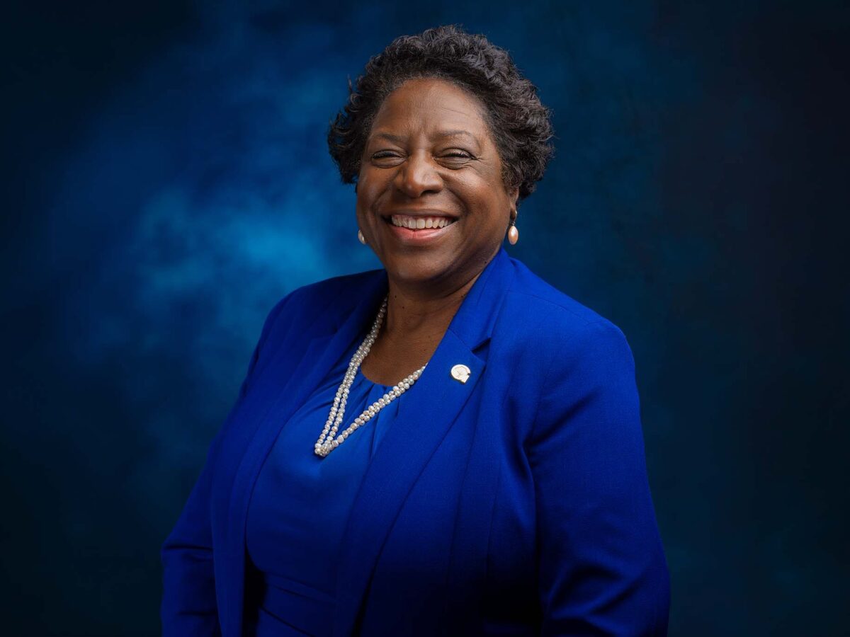 Smiling woman in a royal blue suit against a dark blue studio backdrop.