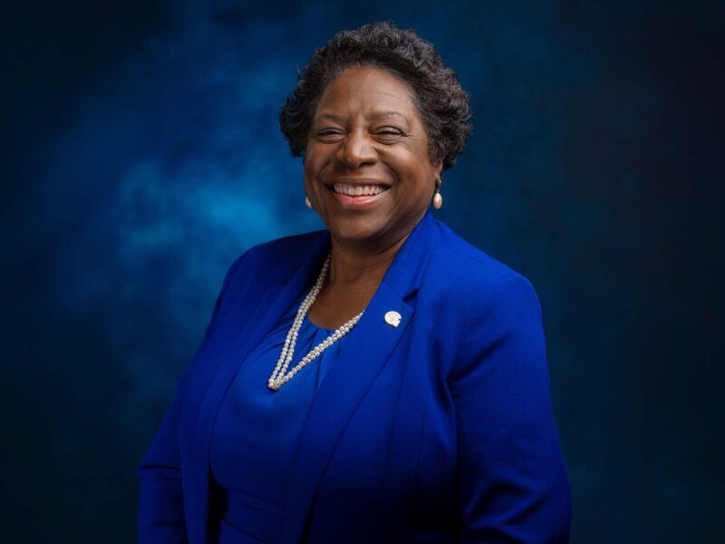 Smiling woman in a royal blue suit against a dark blue studio backdrop.